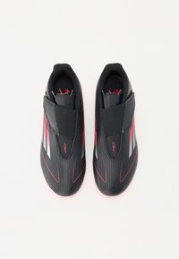 Schwarze Sportschuhe mit einem eleganten Design, ausgestattet mit roten Akzenten und grauen Streifen, aus synthetischem Material mit strukturierter Oberfläche.