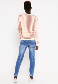 Sudadera a rayas en melocotón y blanco, combinada con jeans skinny azules. El conjunto tiene un diseño casual y se complementa con zapatillas blancas.