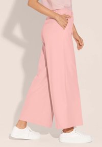 Lichtroze wijde broek met een gladde textuur, voorzien van zijzakken en een aansluitende taille, gecombineerd met witte sneakers.