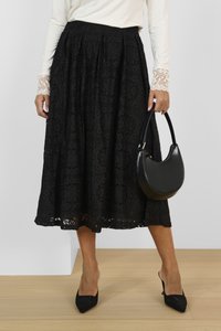 Svart midikjol i spets med blommig utskärning, plisserad design, nederkant med scallop-mönster, kombinerad med en rund svart handväska och spetsiga svarta klackar.