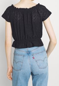 Svart blus med ögla och rynkad off-shoulder halsringning samt elastisk midja, kombinerad med ljusblå högmidjade jeanstights med bakfickor.