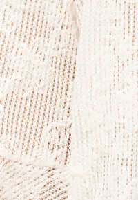 Tissu blanc transparent avec des rayures verticales ajourées et une broderie en dentelle florale créant un motif texturé délicat.