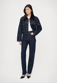Dark denim jacket with a brown faux fur collar, paired with high-waisted dark denim jeans and black high-heeled shoes. Minimalistic design.