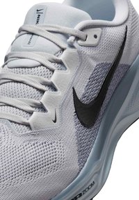Jasnoszary but sportowy wykonany z teksturowanej siateczki, z czarnym logo w kształcie smoka, płaskimi sznurówkami i niebieską gumową podeszwą z detalem "AIR ZOOM".