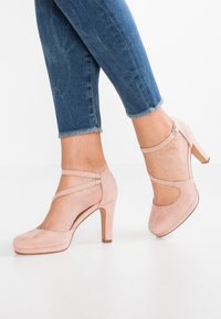 Ljust rosa mocka högklackade skor med rund tå, ankelband och en 10 cm klack, kombinerat med blå denim med fransar.