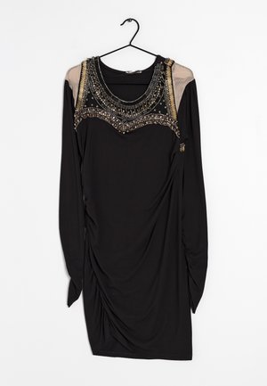 Sort langærmet kjole med transparente beige skulderpaneler og indviklet perlebesat halsudskæring, hængende på en sort bøjle.