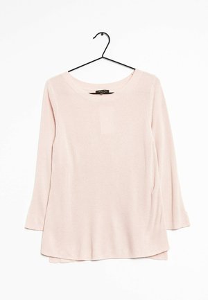Pull en maille rose clair à manches longues avec un col rond, suspendu sur un cintre noir sur fond blanc.