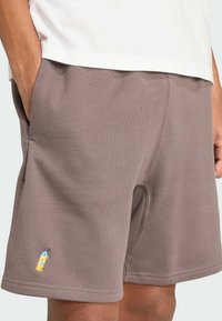 Hnedé šortky z jemného materiálu s bočnými vreckami, na dolnej časti ľavého stehna sú ozdobené vyšívaným designom žltého nápoja.