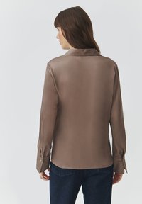 Brown satin long-sleeve shirt with a collar, featuring buttoned cuffs and a smooth texture. Worn with dark denim jeans.