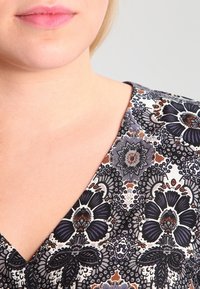 Blumenmusterstoff in dunkelblauen, weißen und rostfarbenen Tönen; verfügt über ein V-Ausschnitt-Design und eine glatte Textur.