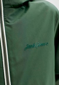 Σκούρο πράσινο μπουφάν με φερμουάρ μπροστά και ανάγλυφο λογότυπο «Jack & Jones» στο αριστερό στήθος.