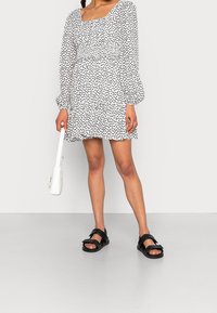 Vestido blanco con lunares negros, corsé fruncido, mangas largas abullonadas y dobladillo rizado. Unas sandalias negras y un pequeño bolso blanco completan el atuendo.