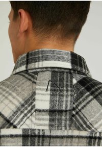 Harmaan ja mustan ruudullinen flanelli-paita, teksturoitu villamateriaali kauluksella ja näkyvillä ompelusyillä takana.