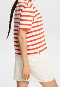 Camisa de rayas roja y blanca de manga corta con un ajuste relajado y aberturas laterales, combinada con una falda de mezclilla de color claro.