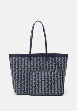 Sac fourre-tout bleu marine en tissu à motif géométrique, avec deux longues poignées et une petite pochette zippée assortie attachée.