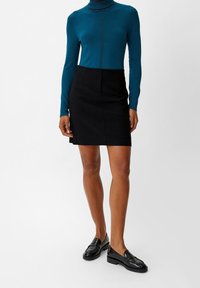 Teal aansluitende coltrui met verticale naden, gecombineerd met een zwarte A-lijn rok. Soepele textuur, kniehoogte, gedragen met zwarte loafers.