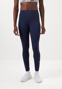 Marineblå højtaljede leggings lavet af strækstof, med et elegant design og et lille hvidt Nike-logo nær anklen.