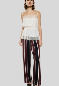 Canotta di seta bianca con pizzo abbinata a pantaloni a vita alta e gamba larga con strisce verticali bordeaux e blu navy.