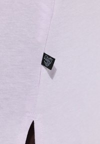 T-shirt in cotone lilla con fessura laterale e etichetta del marchio tessuta nera. La texture è liscia e il design presenta un taglio semplice e classico.