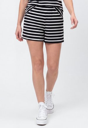 Persoon die zwart-witte horizontale gestreepte korte broek en bijpassende top draagt, lopend in witte hoge sneakers tegen een effen achtergrond.