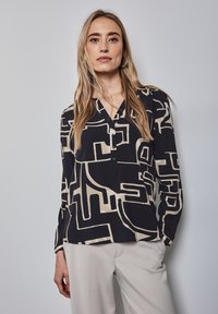 Langärmliges, knöpfbares Hemd in Schwarz und Beige mit abstrakten geometrischen Mustern. Leichter Stoff mit V-Ausschnitt und lockerer Passform.