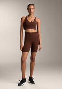 Barna sportmelltartó és magas derekú sort, rugalmas anyagból készült, fekete sportcipővel párosítva. Sima textúra, testhezálló kialakítás.