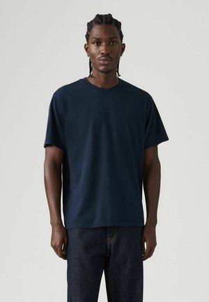 Granatowy bawełniany t-shirt z krótkimi rękawami, okrągłym dekoltem, luźnym krojem, w połączeniu z ciemnymi jeansami, gładką fakturą, bez widocznych wzorów czy logo.