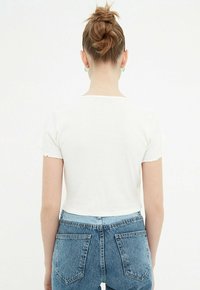 T-shirt bianco a maniche corte e cropped con finitura testurizzata, abbinata a jeans in denim blu a vita alta con tasche posteriori e zip.