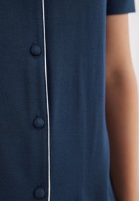 Mörkblå kortärmad skjorta med en mjuk textur, knappslå och vit piping fram för accentuering.