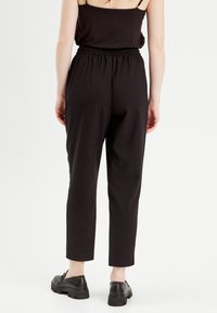 Pantalons en coton noir avec une taille élastique, coupe fuselée et longueur au-dessus de la cheville. Accompagnés de chaussures noires à lacets.
