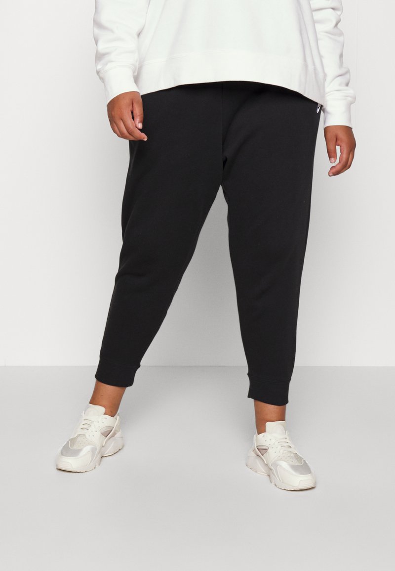 Musta kapenevat collegehousut ribba-äärillä, yhdistettynä valkoiseen huppariin ja vaaleansinisiin lenkkareihin. Yksinkertainen muotoilu, ei näkyviä kuvioita.