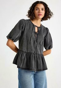 Czarny denimowy top peplum z bufkami, otworem w kształcie klucza i wiązaniem przy szyi. Miękka faktura z widocznymi przeszyciami.