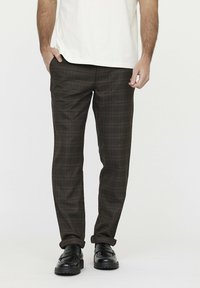 Braun karierte Hosen aus einem Stoff mit glatter Textur. Sie haben eine schmale Passform und umgeschlagene Säume, kombiniert mit schwarzen Schuhen.