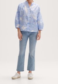 Chemise à motifs floraux bleu clair avec un col mandarin et des manches amples, associée à un jean évasé bleu clair et des baskets blanches.