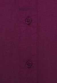 Maroon fabric with a textured finish, featuring a button detail with four holes. Close-up of shirt or garment with vertical seam lines.