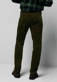 Spodnie sztruksowe w kolorze oliwkowej zieleni, z pięcioma kieszeniami, o prostym kroju i widocznymi przeszyciami. Noszone z niebiesko-zieloną kratowaną koszulą.