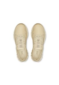 Beige sportssko med en tekstureret overdel, snørelukning og kraftig sål. Har logo branding på siden og blødt stoffor.