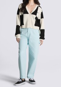 Černo-bílý vzorovaný kardigan, krátký střih s výstřihem do véčka, doplněný světle modrými kalhotami a černými teniskami s bílými detaily.