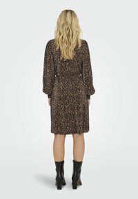 Obleka z leopardjim vzorcem, dolgimi rokavi, ožjim pasom, dolžino do kolen in mehko blago; v kombinaciji z črnimi gležnjarji.