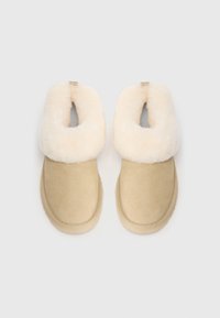 Chaussons en daim beige avec de larges collerettes en fourrure couleur crème, conçus pour la chaleur et le confort, vus de dessus sur un fond blanc.