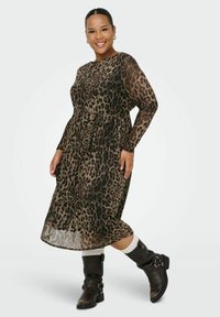 Vestito midi a stampa leopardata con maniche lunghe, vita regolabile con cordino e sovrapposizione trasparente, abbinato a stivali alti neri fino al ginocchio e calzini bianchi.