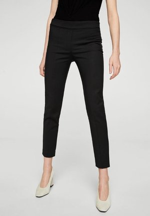 Black fitted pants with a high waistband, tapered legs, and a smooth texture. Worn with light-colored heels. Simple and sleek design.