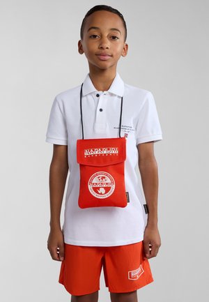 Röd tygpåse med klaff, logodetaljer och nackrem, bärs över en vit polo och orange shorts. Texturerad yta och sömlöst design.