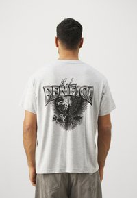 Pilkas medvilninis marškinėlis su juoda erelio grafika ir užrašu "S.L. BENFICA" ant nugaros. Trumpomis rankovėmis, laisvas kirpimas.