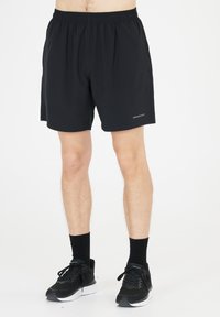 Sorte atletiske shorts lavet af letvægtsstof, med et elastisk taljebånd og sidelommer. Båret med sorte sneakers og sokker.