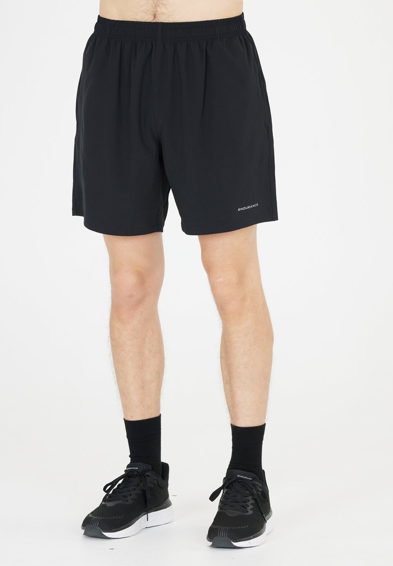 Sorte atletiske shorts lavet af letvægtsstof, med et elastisk taljebånd og sidelommer. Båret med sorte sneakers og sokker.