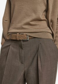 Bruin gebreid truitje gecombineerd met bruine geplooide broek. Een gevlochten bruine riem met een metalen gesp voegt detail toe. Zachte texturen en aardetinten.