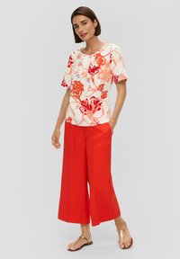 Bloemendessert kort mouwen top met rode, roze en blauwe patronen; gecombineerd met wijde rode broek; gestyled met platte metallic sandalen.