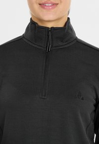 Zwarte kwart-rits pullover gemaakt van textuurstof, met een opstaande kraag en een klein logo op de linkerkant van de borst.