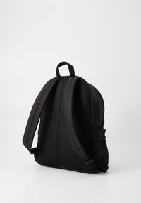 Sac à dos noir avec une finition en tissu lisse et un panneau arrière texturé. Il dispose de bretelles rembourrées et d'une poignée supérieure pour le transport.